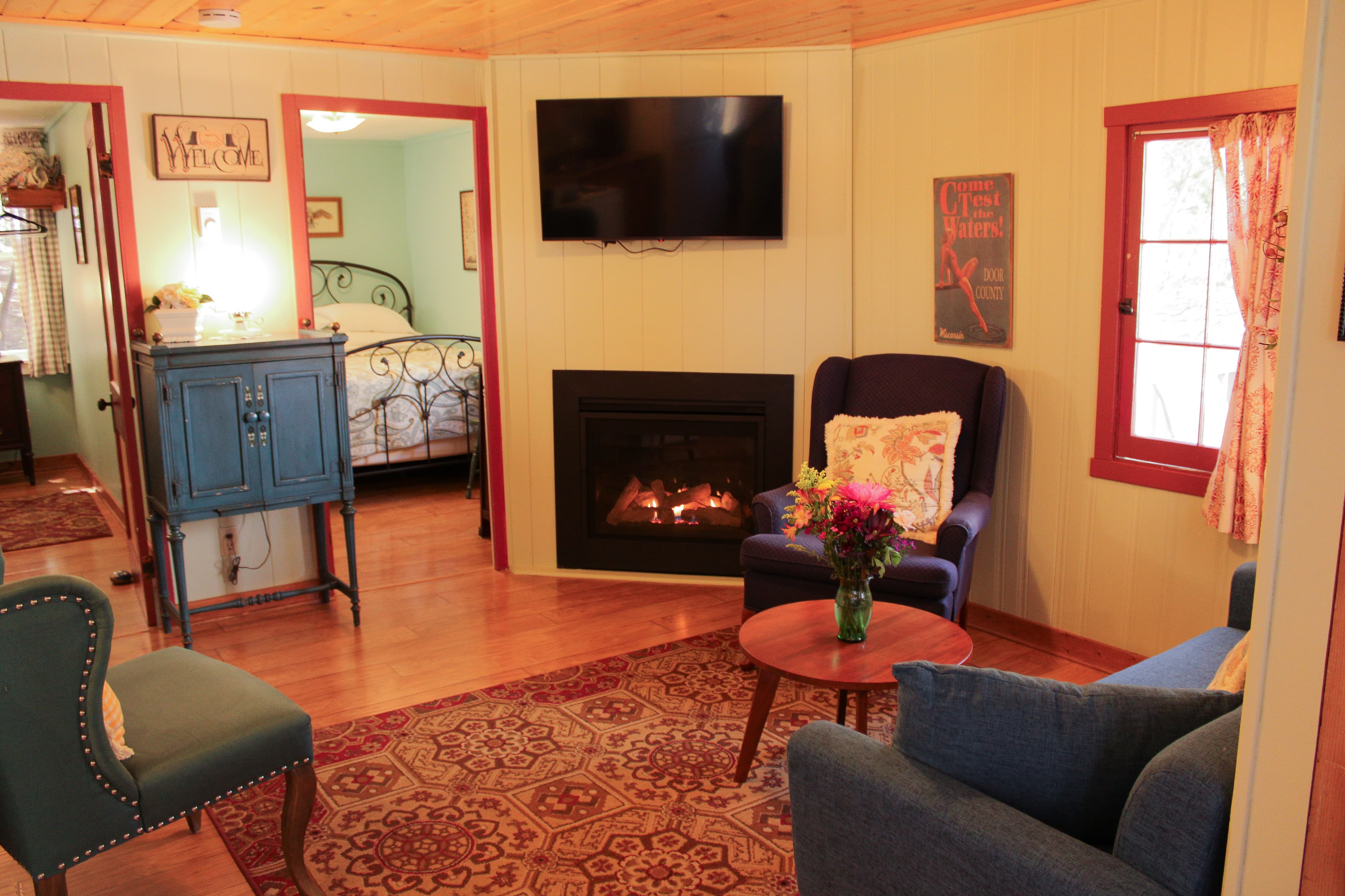 A charming cottage interior with wood-paneled ceilings, a cozy living room with a fireplace, and views into two adjoining bedrooms.