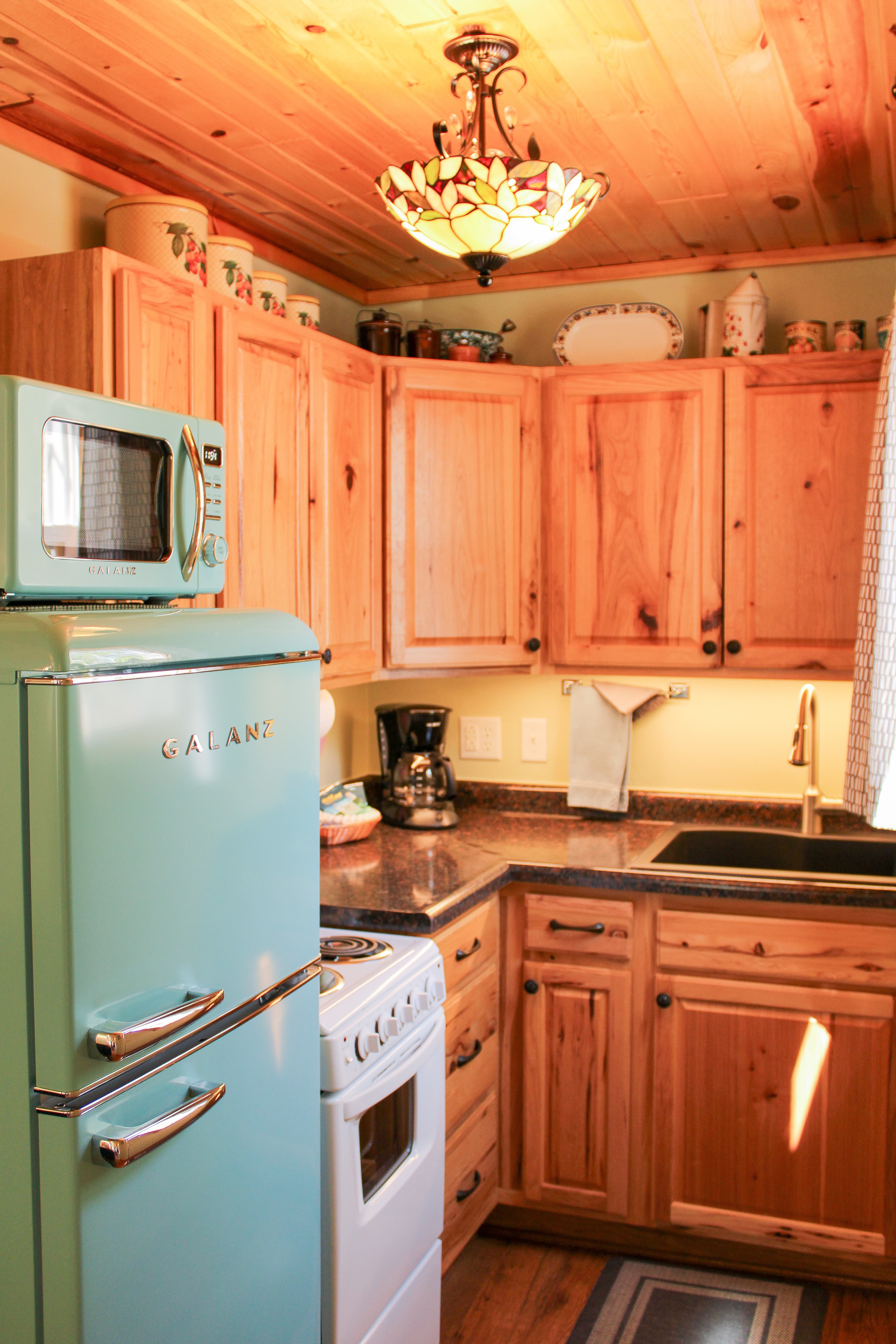 A functional kitchen featuring wooden cabinets, a black sink, a white stove, and a small refrigerator, with a wood-paneled ceiling.