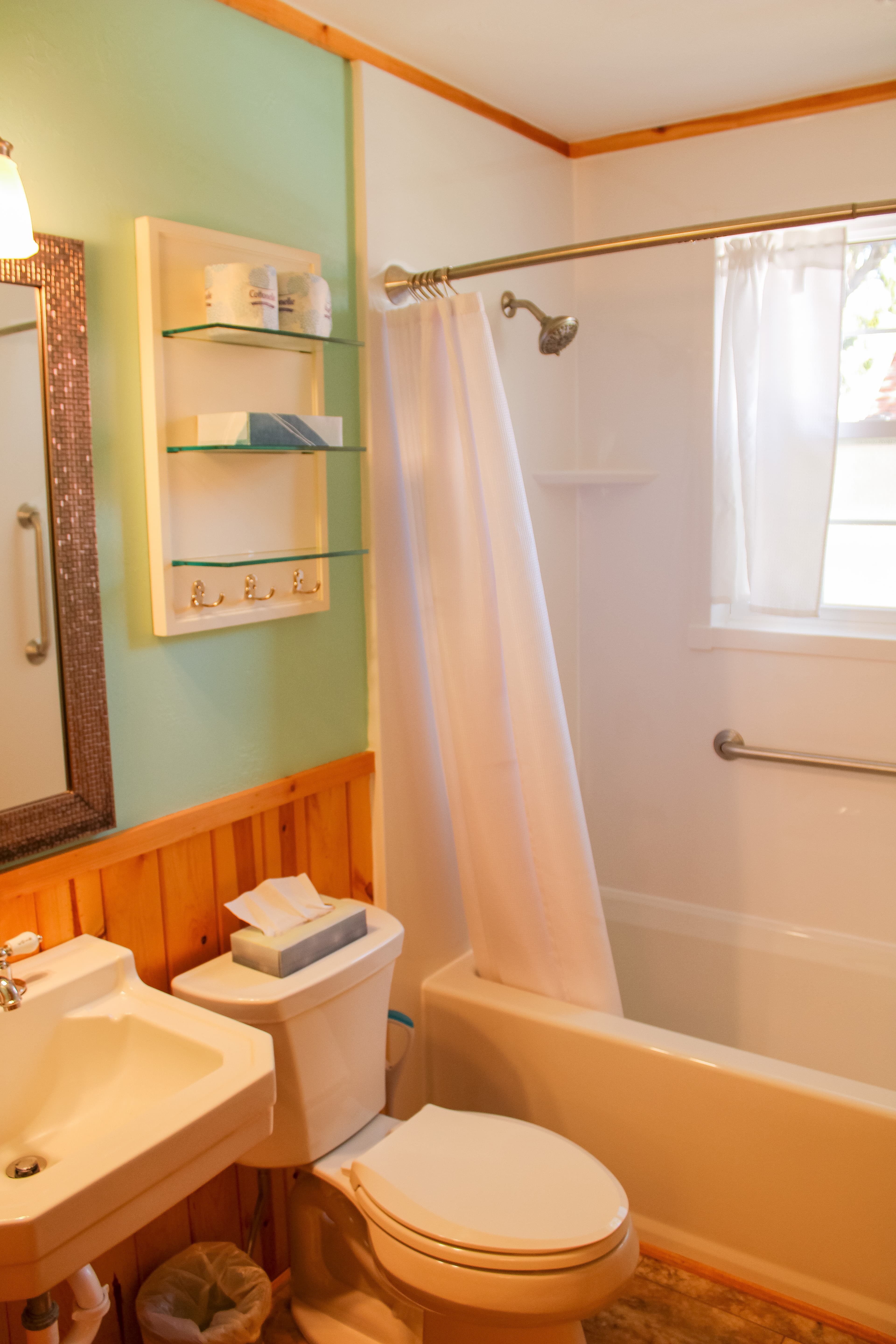 A roomy bathroom featuring light green walls, wood paneling, a white sink and toilet, and a bathtub with a white shower curtain.