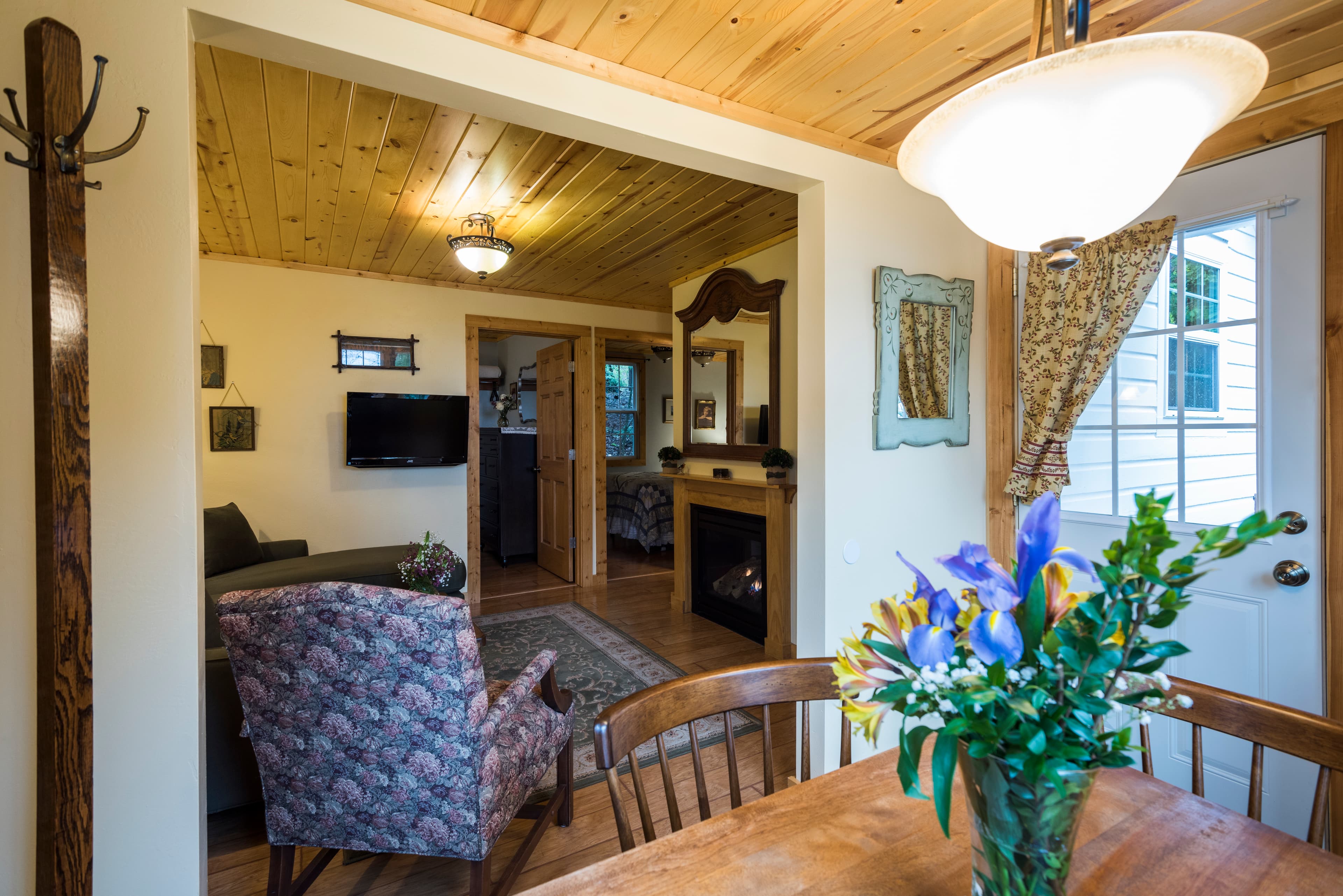 A charming interior view featuring a rustic dining area with a vase of flowers, opening into a cozy living room with a fireplace.