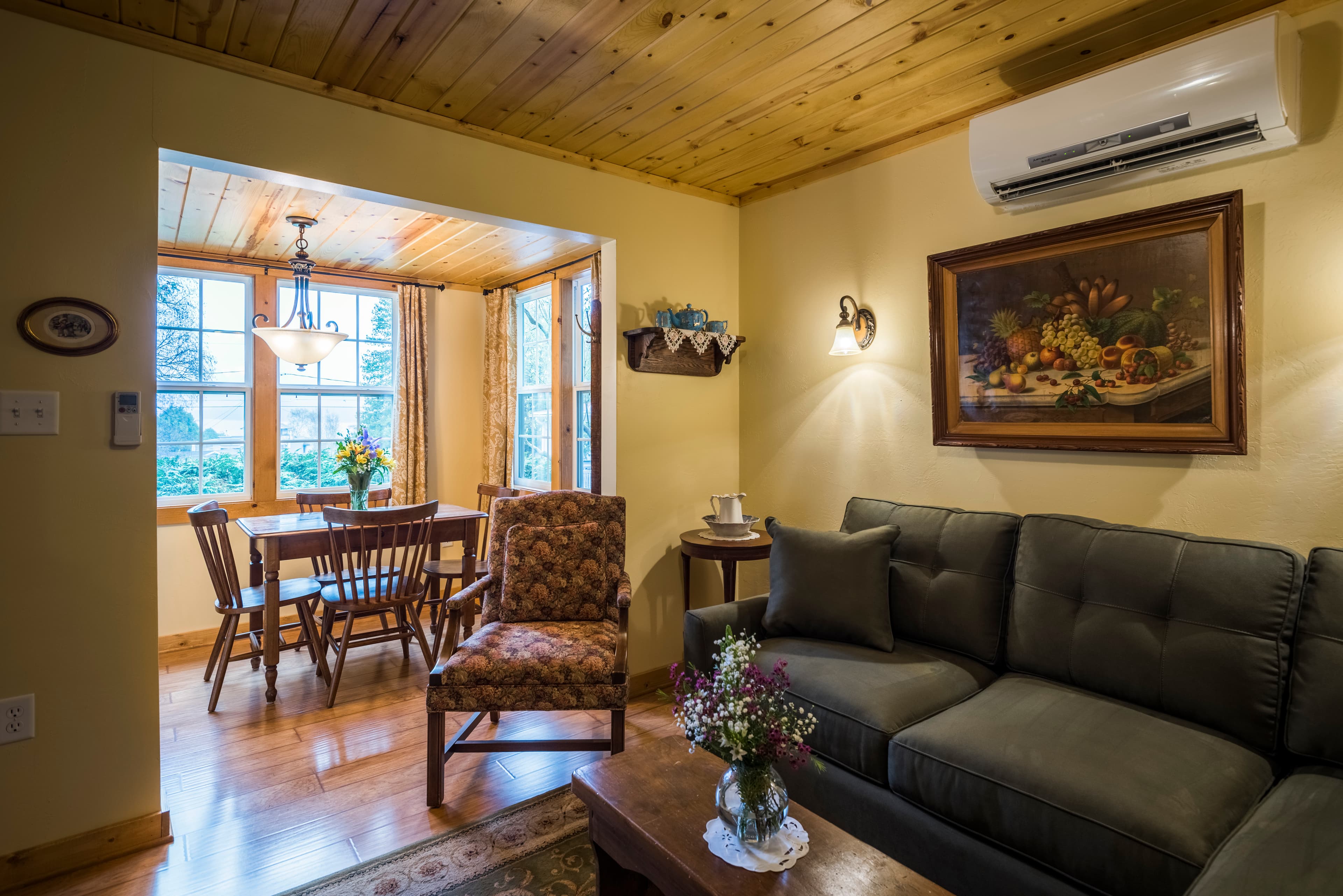 A spacious living room with a green sectional sofa, a fireplace with a mirror above it, and two open doorways leading to other rooms.