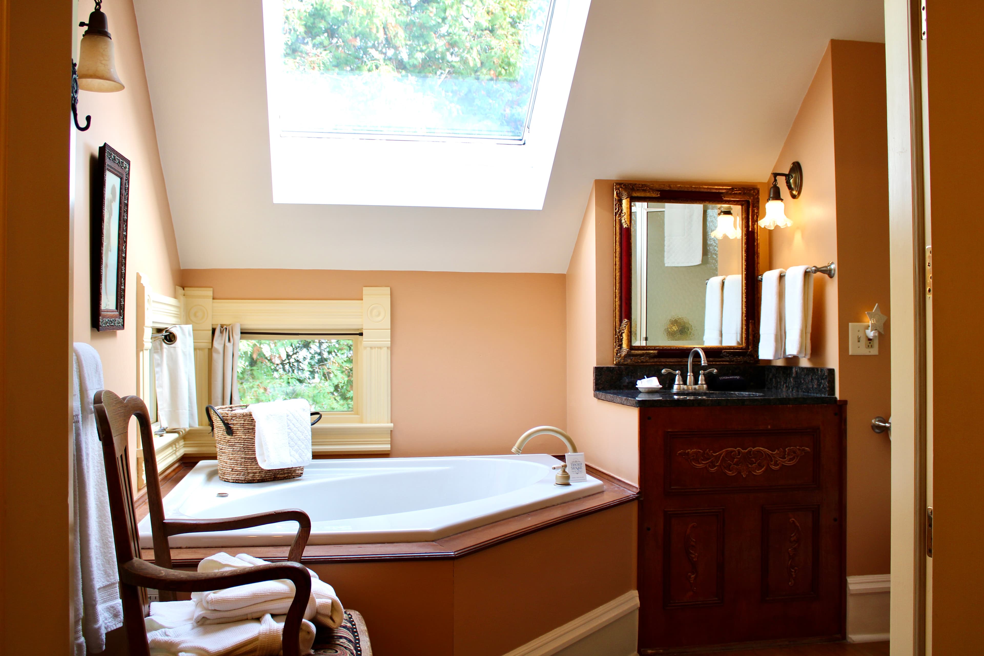 A well-lit bathroom with a large corner spa tub, a skylight, and a wooden vanity, all with a cozy and inviting ambiance.