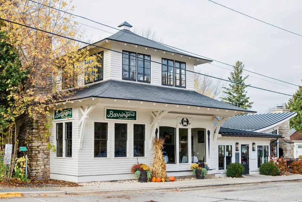 A white, two-story building with large windows and a sign reading "Barringers" surrounded by autumn foliage and decorative pumpkins.