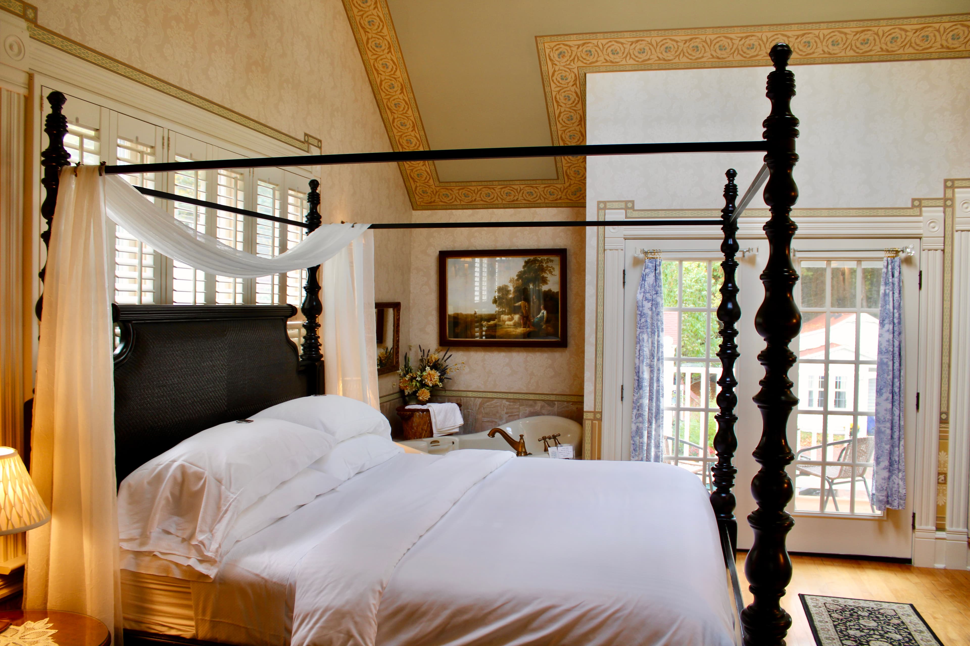 A bright and airy bedroom featuring a four-poster bed, elegant decor, and large windows with views.