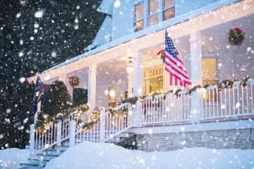 A snowy porch adorned with holiday lights and an American flag.