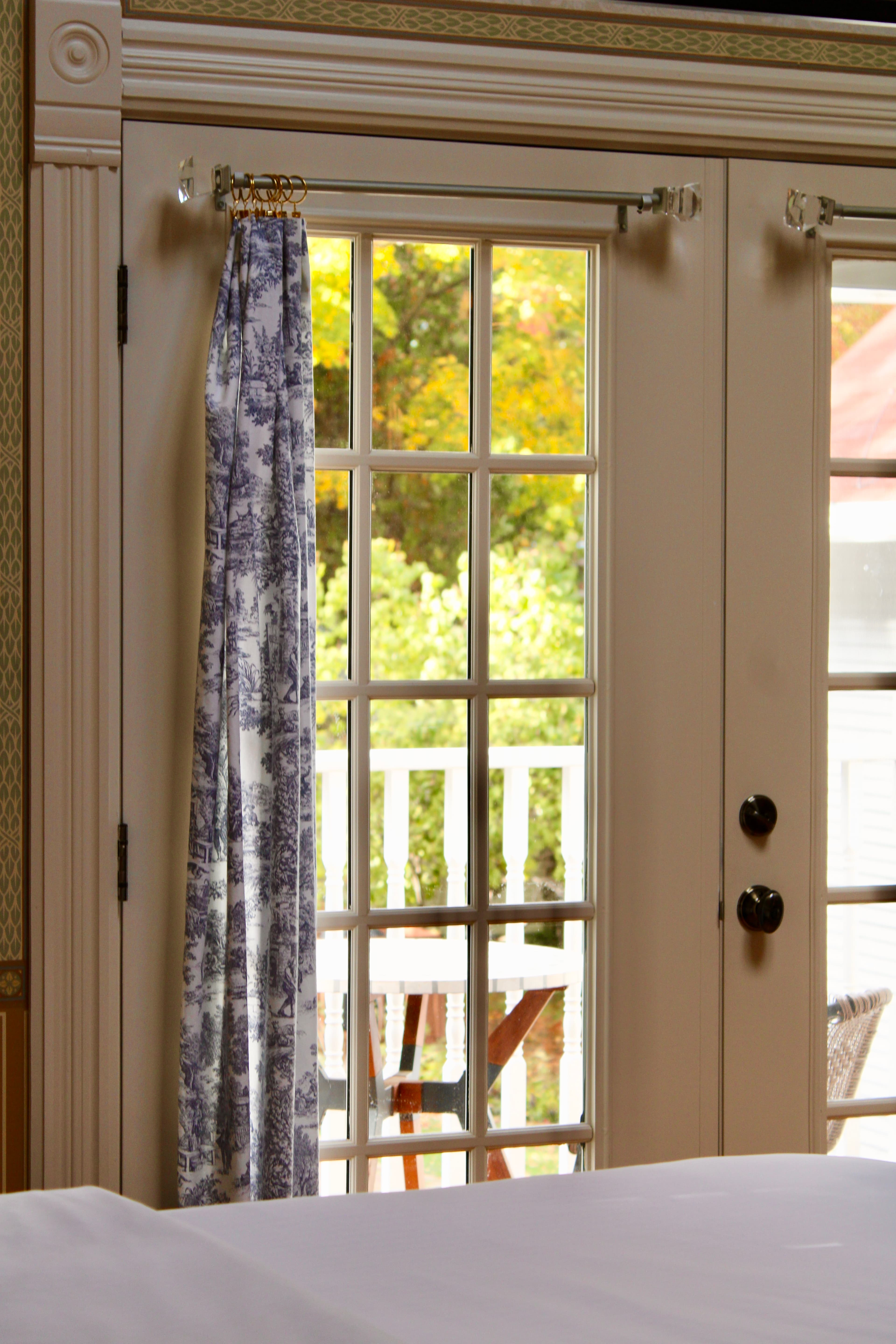A view of double doors with a blue-patterned curtain, opening to a lush outdoor area.