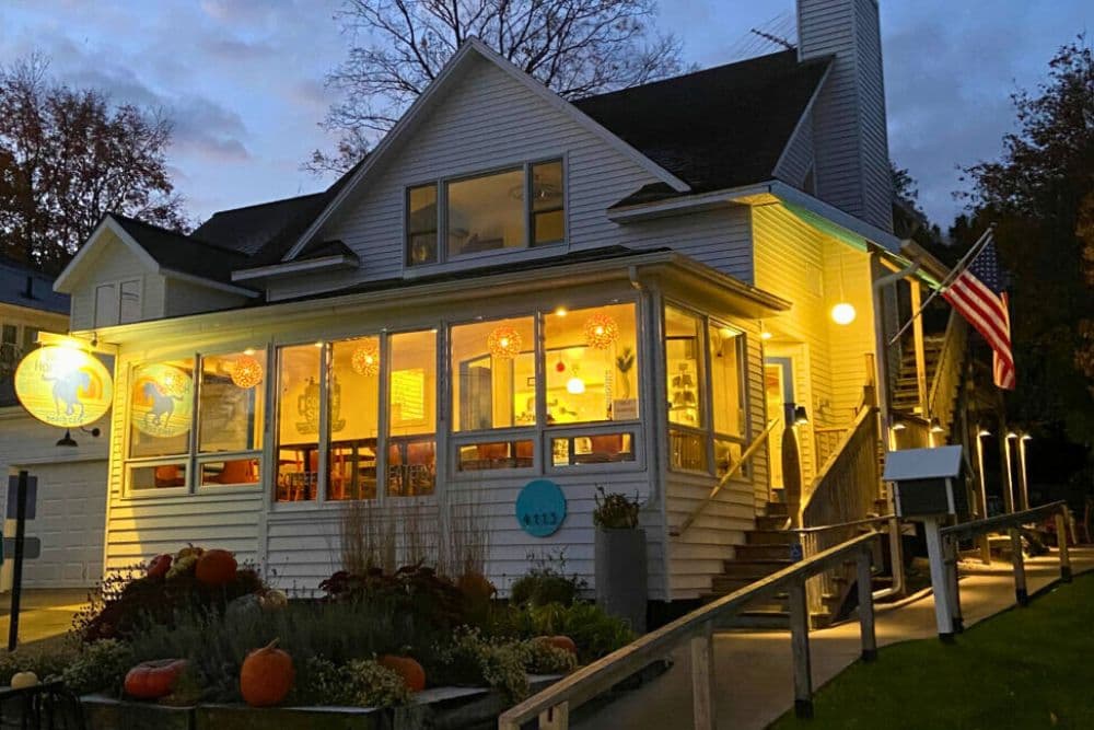 A cozy, illuminated building with large windows, featuring pumpkins and an American flag outside.