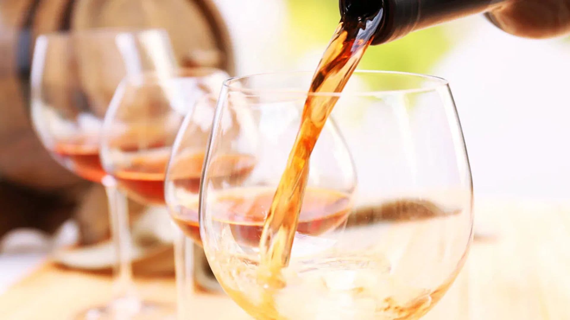 A glass is being filled with amber liquid from a bottle, with additional empty glasses in the background.