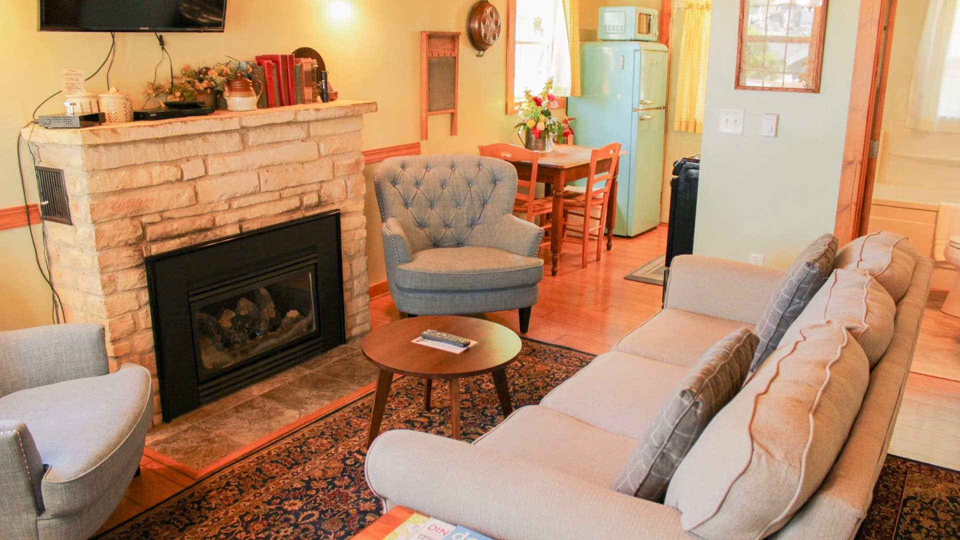 Cozy living area featuring a stone fireplace, comfortable seating, and a dining space with a vintage refrigerator.