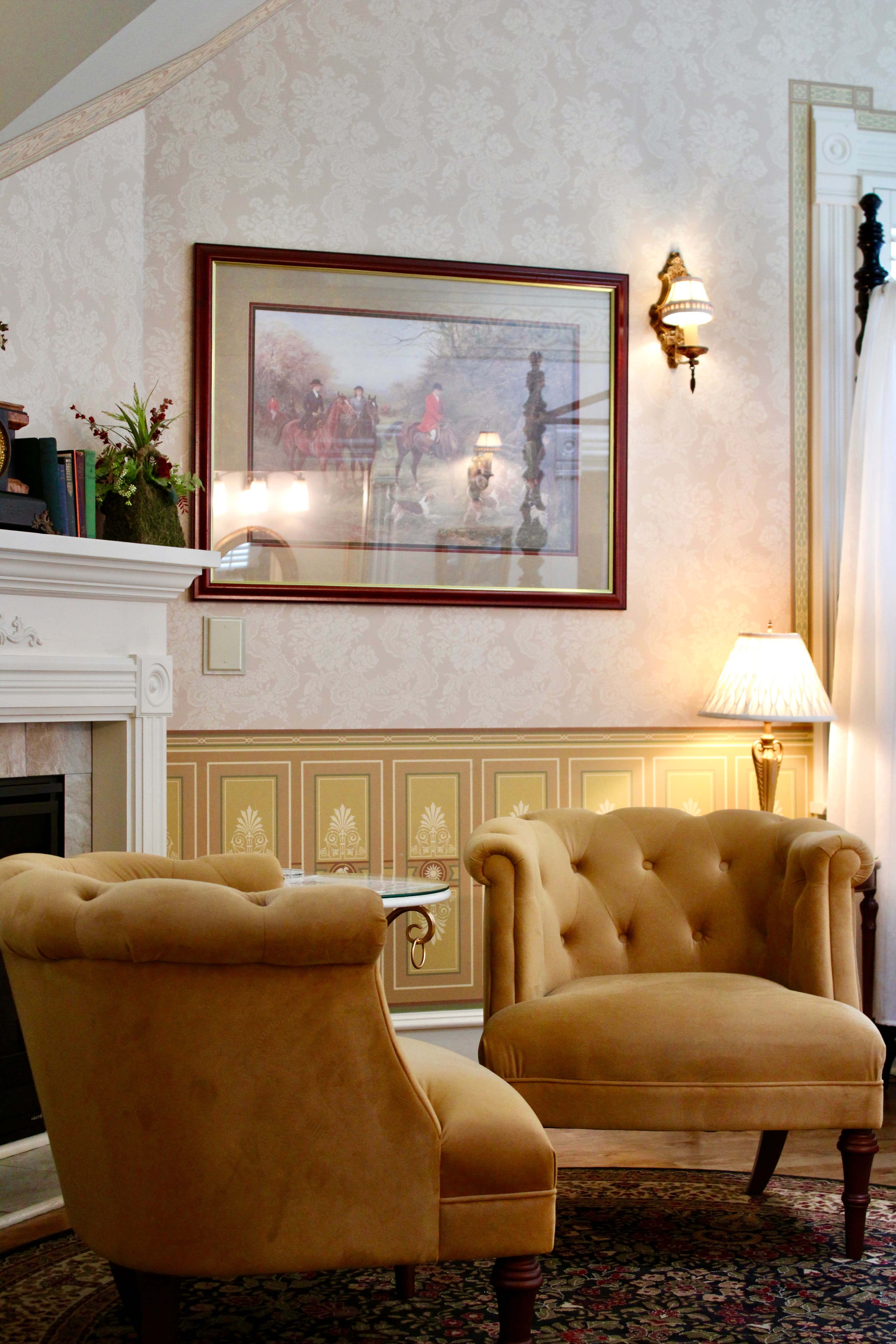 A cozy living space featuring two tufted beige chairs, a small table, and a decorative wall painting.