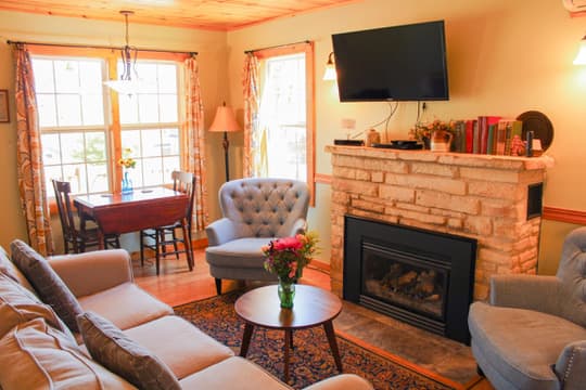 A welcoming living room with a stone fireplace, a wall-mounted TV, a blue armchair and sofa, and warm wood-paneled ceilings.