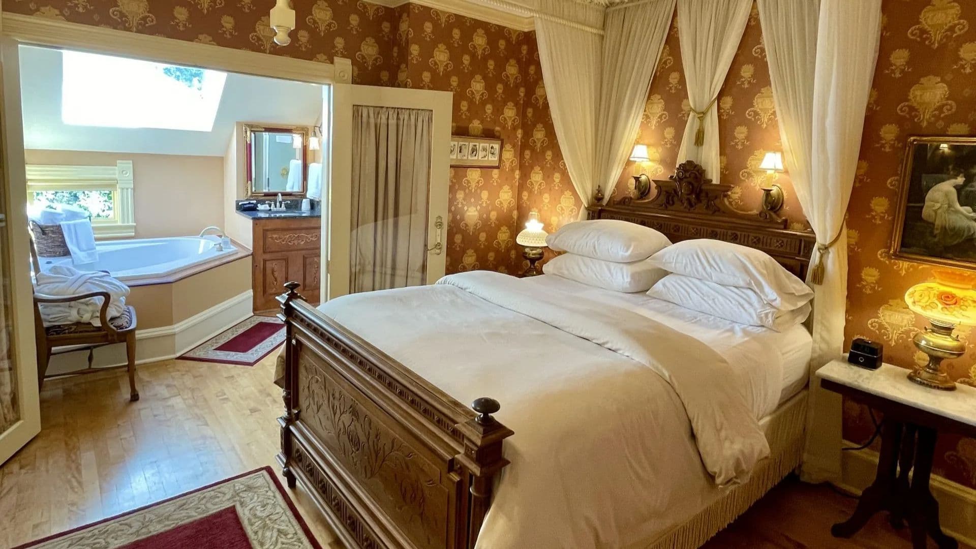 A beautifully decorated bedroom featuring a wooden bed, elegant wallpaper, and an attached bathroom with a bathtub.