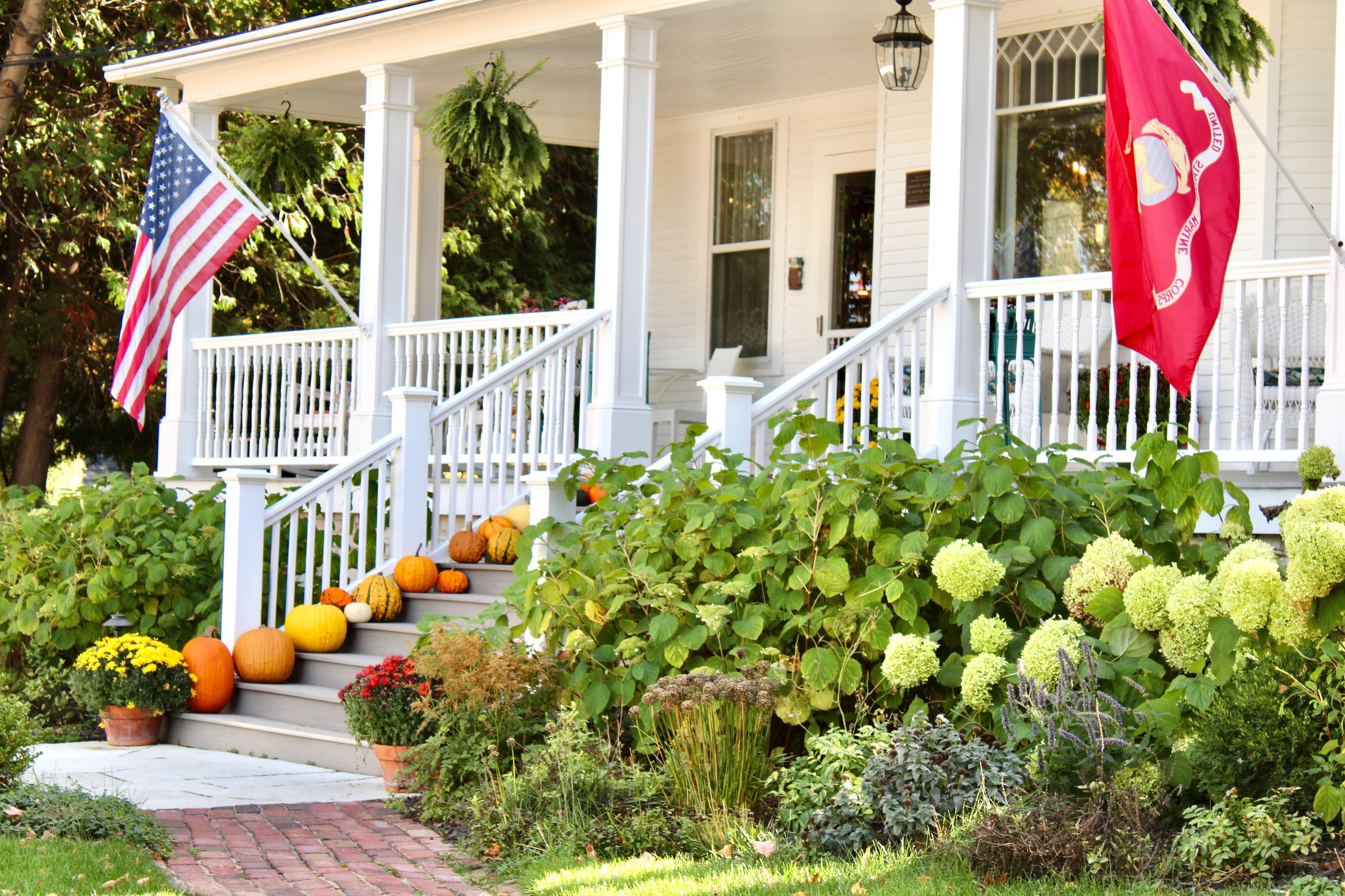 A welcoming porch adorned with an American flag, a red flag, pumpkins, and vibrant autumn plants. A welcoming porch adorned with an American flag, a red flag, pumpkins, and vibrant autumn plants.
