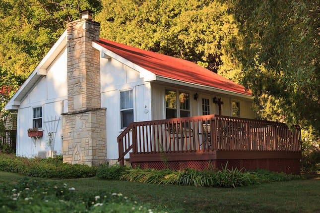 A cozy cottage with a red roof and wooden deck surrounded by greenery. A cozy cottage with a red roof and wooden deck surrounded by greenery.