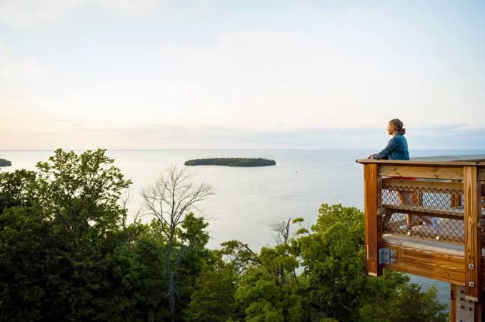 A person sits on a wooden deck overlooking a calm lake with an island in the distance.
