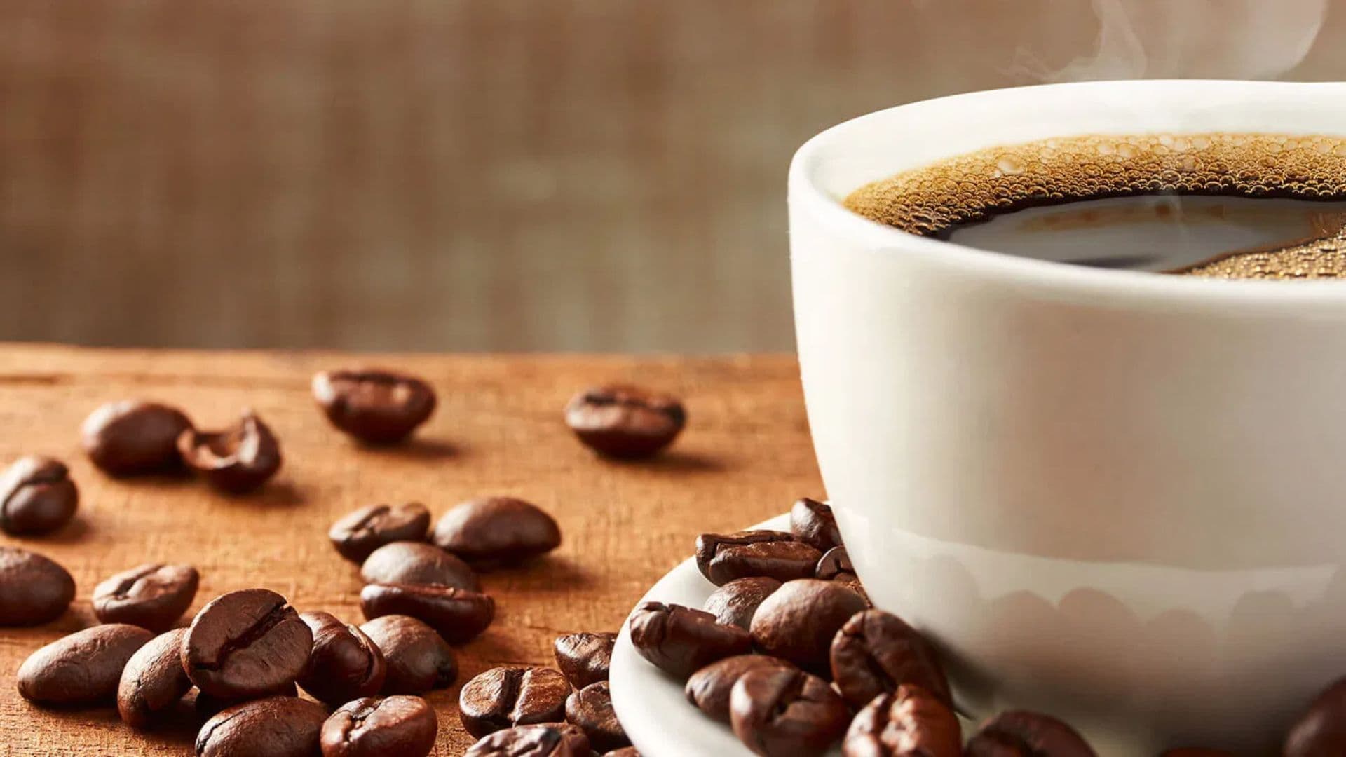A steaming cup of black coffee surrounded by scattered coffee beans on a wooden surface.