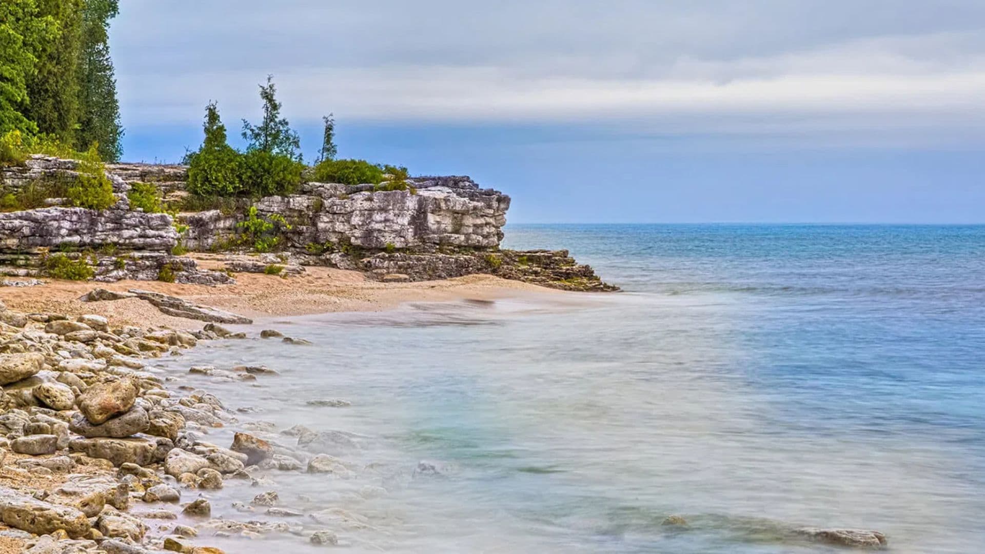 Rocky shoreline meeting a calm, blue lake under a cloudy sky.