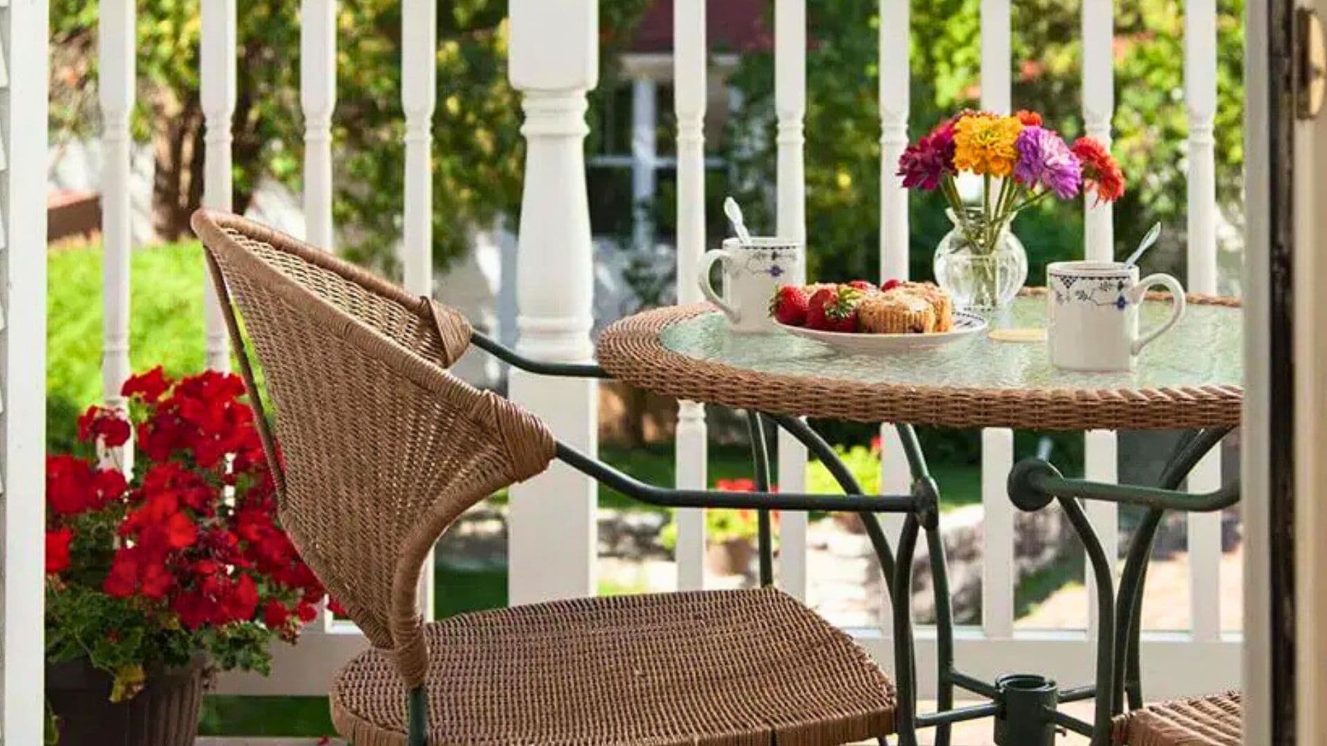 A cozy balcony setup featuring a table with a vase of flowers, cups, and a plate of snacks.
